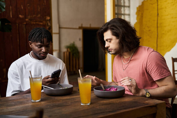 Два красивых мужчины делят интимный момент в кафе, наслаждаясь едой и беседой.