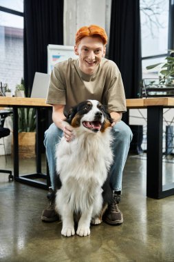 Kızıl saçlı genç bir adam modern ofis alanında köpeğiyle vakit geçirmekten hoşlanıyor..