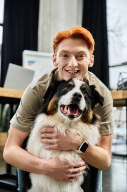 Kızıl saçlı genç adam modern ofis ortamında çalışırken bir köpekle sıcak bir anı paylaşıyor.