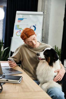 Hareketli bir ofis ortamında, genç kızıl saçlı bir adam görevlerini yerine getirirken köpeğiyle meşgul olur..
