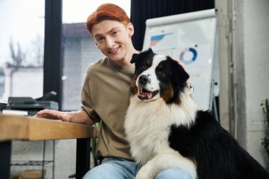 Canlı kızıl saçlı genç bir adam modern bir ofiste işini seviyor, şirin bir köpekle yer paylaşıyor..