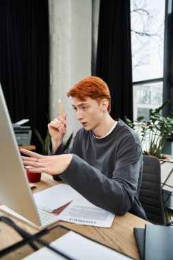 Kızıl saçlı kendini adamış genç adam, çağdaş bir ofis çalışma alanında iş birliği yapıyor..