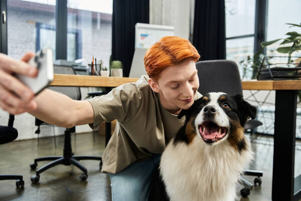 A young red haired man happily interacts with his friendly dog while working in an office.