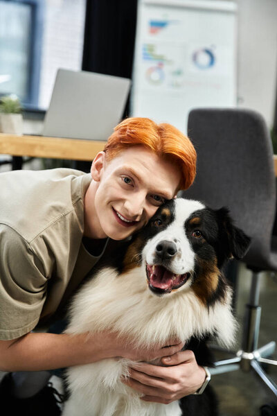 A young red haired man shares a joyful moment with a cheerful dog in a bright office environment.