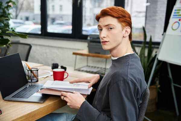 Focused young man with red hair engages with tasks at a contemporary office workspace.