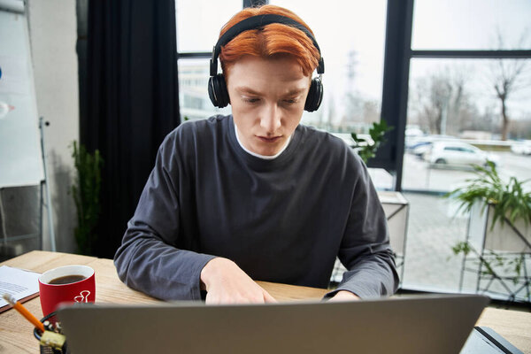 Red haired young professional works productively at his desk in a stylish office.