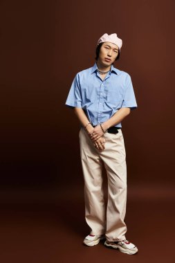 Genç Asyalı adam, moda anlayışını, şık bir kıyafetle, sıcak bir arka planda sergiliyor..