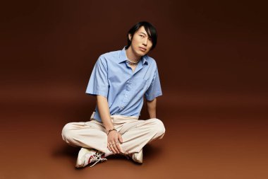 Genç bir adam şık bir stüdyoda rahatça otururken moda anlayışını sergiliyor..