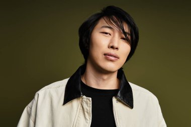 Genç Asyalı adam stüdyo ortamında kendine güvenen bir pozla şık kıyafetini sergiliyor..