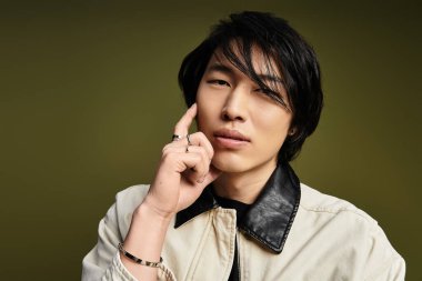 Genç Asyalı bir adam yaratıcı bir stüdyo ortamında modern modanın altını çizerek düşünceli bir şekilde poz veriyor..