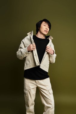 Genç Asyalı bir adam kendine güvenerek stüdyoda poz veriyor, modaya uygun bir kıyafet ve eşsiz bir stil sergiliyor..