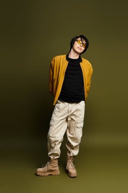 Genç bir Asyalı, kendine güvenen bir şekilde stüdyoda poz veriyor, modaya uygun bir kıyafet ve eşsiz bir tarz sergiliyor..