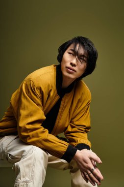 Moda kıyafetleri içindeki genç adam stüdyoda rahat ama şık bir poz sergiliyor..