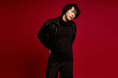 Siyahlı şık Asyalı genç adam kırmızı arka planda poz veriyor..