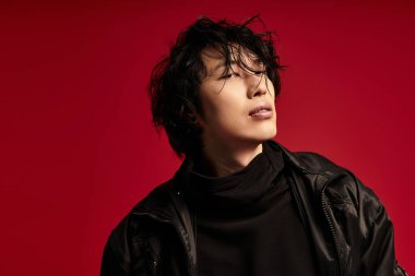 Kırmızı stüdyoda siyah kıyafetli yakışıklı Asyalı poz veriyor.