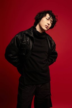 Havalı siyah elbiseli yakışıklı genç bir adam canlı kırmızı bir arka plana karşı duruş sergiliyor..