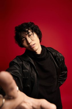 Siyah saçlı, ceketli ve balıkçı yakalı Asyalı adam kırmızıya karşı duruyor..