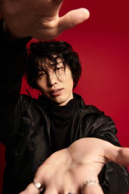 Asyalı model, ellerini uzatarak kırmızı bir arka plana doğru poz veriyor..