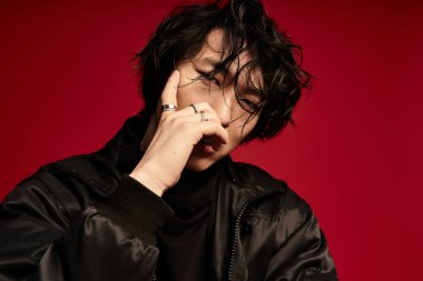 Siyah ceketli genç bir Asyalı stüdyoda şık poz veriyor. Düşünceli ve şık görünüyor..