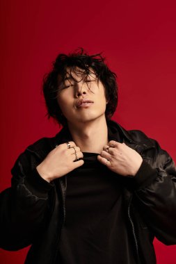 Kırmızı stüdyoda Asyalı bir adam, şık poz veriyor, yakasını düzeltiyor..