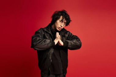 Kırmızı bir stüdyoda poz veren siyah elbiseli şık bir genç..