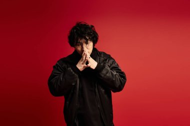 Siyahlı şık Asyalı adam ellerini kırmızı üzerine koyup poz veriyor..