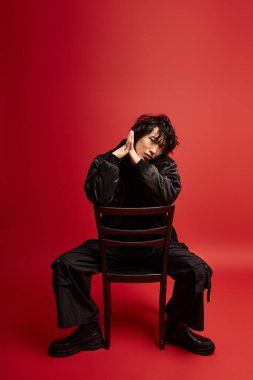 Genç Asyalı bir adam arka koltukta oturur siyah bir elbise giyer kırmızı bir fona karşı.