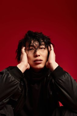 Şık saçlı Asyalı bir adam, şık bir kıyafet giyiyor, stüdyo ortamında dramatik bir şekilde poz veriyor..