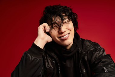 Genç Asyalı bir adam kırmızı stüdyo ortamında şık bir poz veriyor..