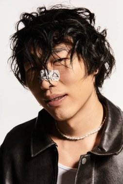 Genç, modaya uygun Asyalı bir adam beyaz bir stüdyo ortamında şık bir poz veriyor..