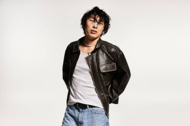 Stüdyodaki şık Asyalı adam deri ceket ve modern giysilerle poz veriyor..