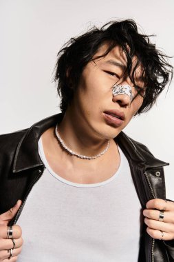 Burnu alçılı Asyalı bir adam stüdyo ortamında siyah ceket ve inci kolye takıyor..