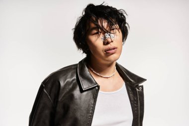 Burnu alçılı, şık giyinmiş genç Asyalı bir adam stüdyoda poz veriyor..