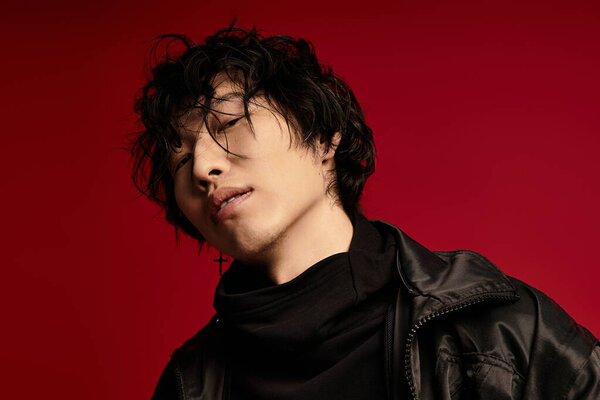 Young, asian man with dark hair poses in a studio. He wears a stylish jacket and a dark turtleneck.
