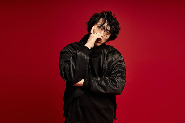 Young asian man in fashionable black outfit thoughtfully poses in front of a bold red backdrop.