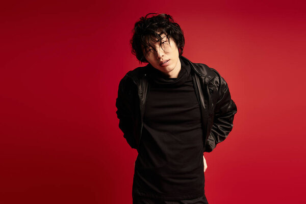 Молодой азиат с грязными волосами, одетый в черное позирует на красном фоне..
