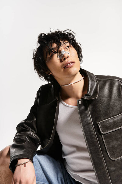 An asian man models in a studio with stylish clothes. He has a plaster on nose and gazes upwards