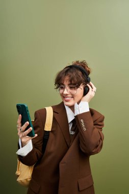 Şık giyinen kendine güvenen genç bir kadın kulaklık dinlerken telefonunu kontrol ediyor..