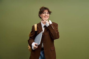 Şık genç bir kadın dizüstü bilgisayarla poz veriyor, şık kıyafetiyle sessiz bir arkaplanda hava atıyor..