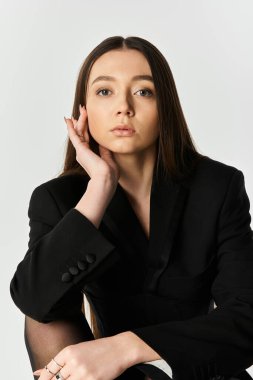 Uzun saçlı genç bir kadın beyaz bir arka fona karşı şık bir şekilde poz veriyor..