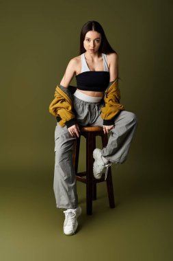 Genç ve güzel bir kadın, kendine güvenerek bir tabureye oturur, şık kıyafetleriyle ve modern yeteneğiyle hava atar..