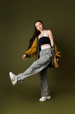 Genç bir kadın, sessiz bir arkaplanda modern kıyafetler sergilerken kendine güvenen bir poz veriyor..