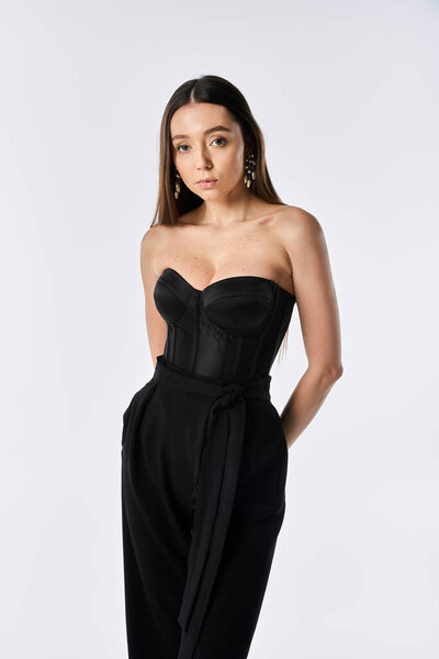 Молодая женщина уверенно моделирует модный наряд на простом фоне.