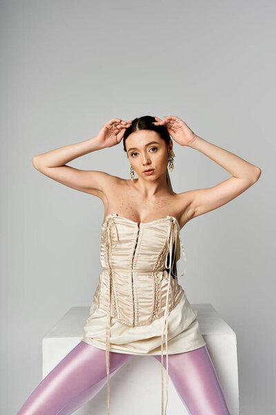 Trendy young woman playfully poses in a stylish outfit within a minimalistic setting.