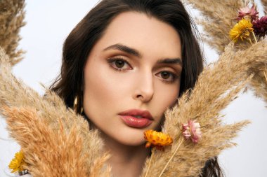 Renkli çiçeklerle çevrili güzel bir genç kadın bir stüdyoda bahar zamanı cazibesini yayıyor..