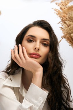 Dalgalı kahverengi saçlı güzel bir kadın zarif poz veriyor, canlı çiçeklerle çevrili..