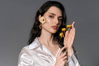 Kahverengi saçlı güzel bir kadın canlı bahar çiçekleri arasında zarafetle poz veriyor..