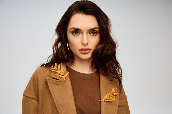 Красивая молодая женщина с длинными каштановыми волосами изящно стоит в пальто с натуральными элементами
