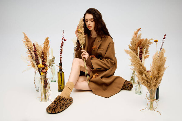 Молодая женщина с длинными каштановыми волосами расслабляется среди цветущих цветов в светлой весенней обстановке.