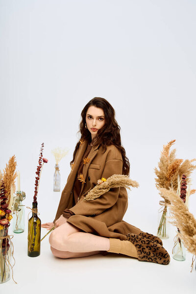 Молодая женщина с длинными каштановыми волосами носит уютное пальто, наслаждаясь цветами вокруг нее.